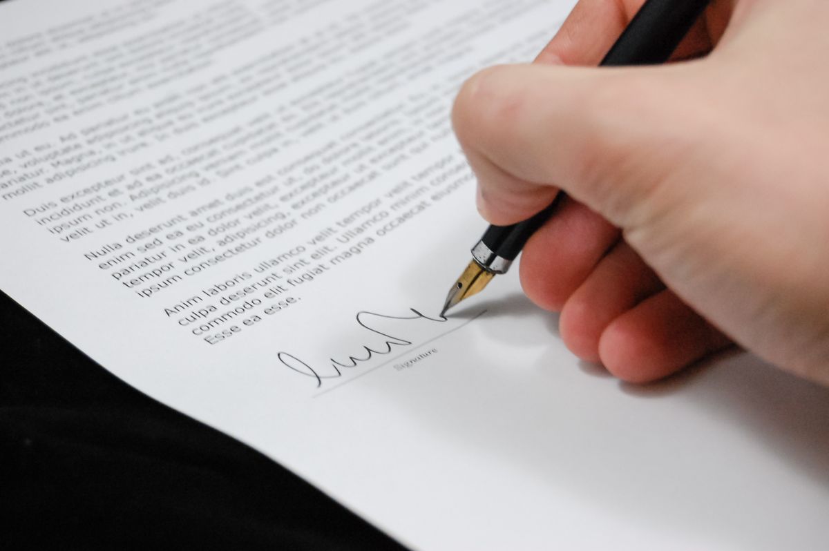 Pessoa assinando documento legal com caneta, representando contrato de trabalho