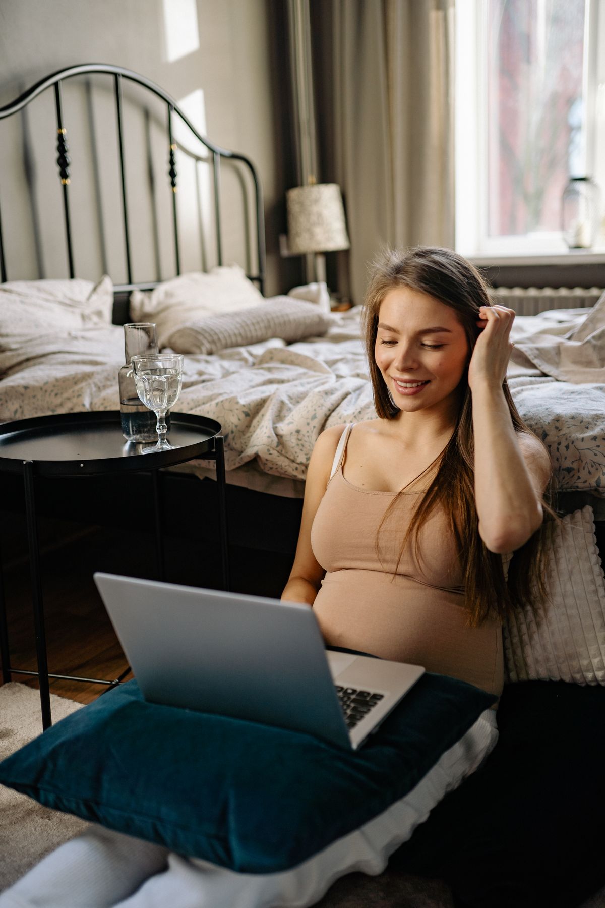 Gestante sorridente usando laptop em casa, conciliando gravidez e trabalho